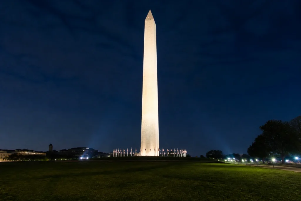 Washington Monument illuminated above its grounds at night